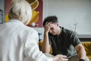A young man in a therapy session, expressing emotions with hand on forehead.